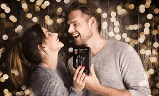 Na zdjęciu widzimy uśmiechnięta parę, która stoi blisko siebie trzymając w dłoniach grę ,,Arkana Miłości''. Tło to drewniana tekstura z wieloma okrągłymi efektami świetlnymi.