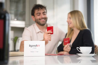 Na obrazku widzimy zakochaną parę siedzącą blisko siebie przy oknie. Kobieta siedzi na kolanach mężczyzny, a ich interakcja wydaje się być bardzo bliska.