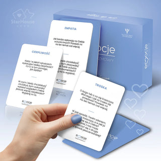 Kobieca dłoń paznokcie pomalowane na niebiesko trzymająca karty do gry Emocje Nasze Rozmowy z prezentacją niebieskiego opakowania gry na neutralnym tle. 